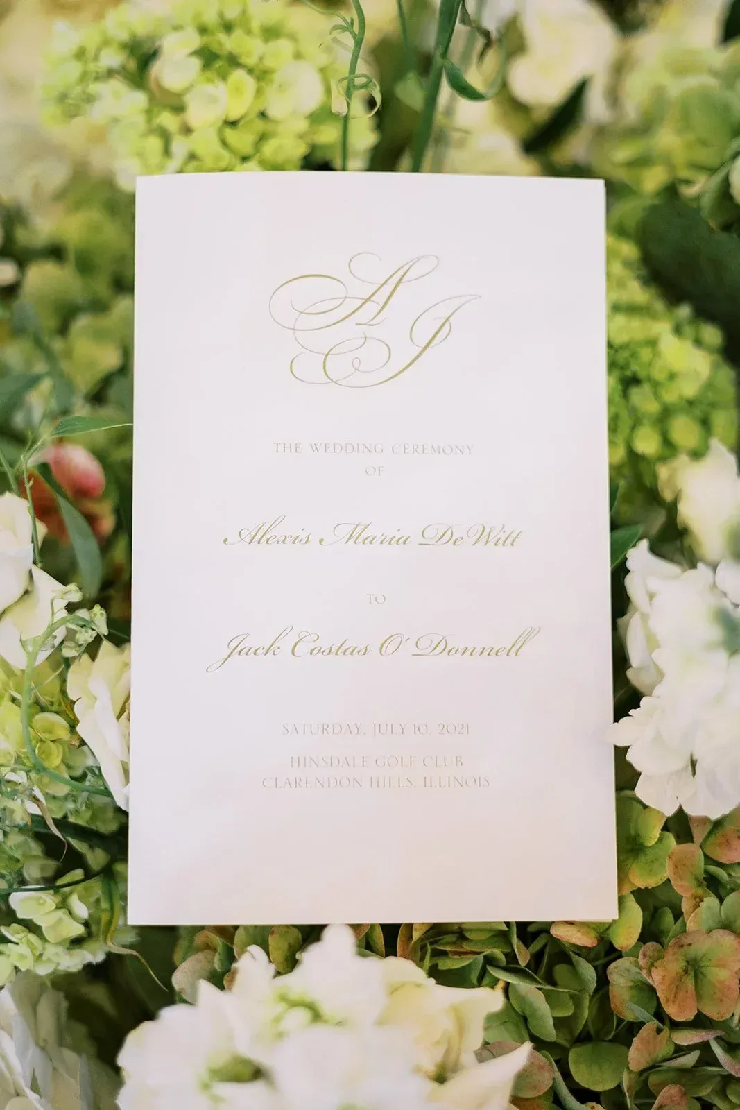 Ceremony program with gold monogram held against hydrangeas