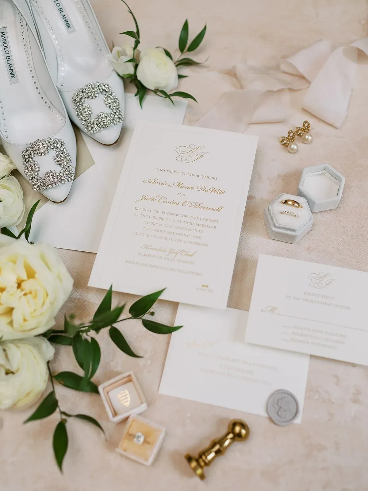 Ivory invitation suite with a gold script monogram, styled with bridal shoes and greenery